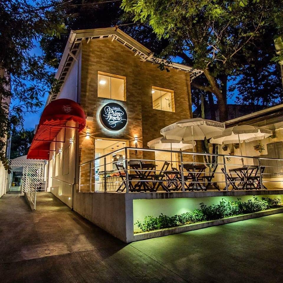Fachada da Gelateria Primo Amore à noite, com o deck iluminado e guarda-sóis