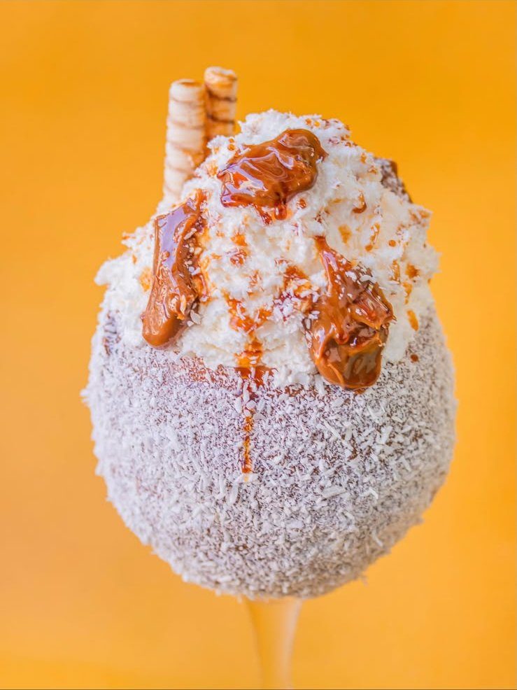 Taça com raspas de coco, doce de leite e canudos sobre fundo amarelo