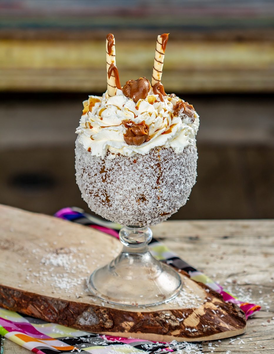 Taça Doce Vida coberta de doce de leite e raspas de coco, com dois canudos
